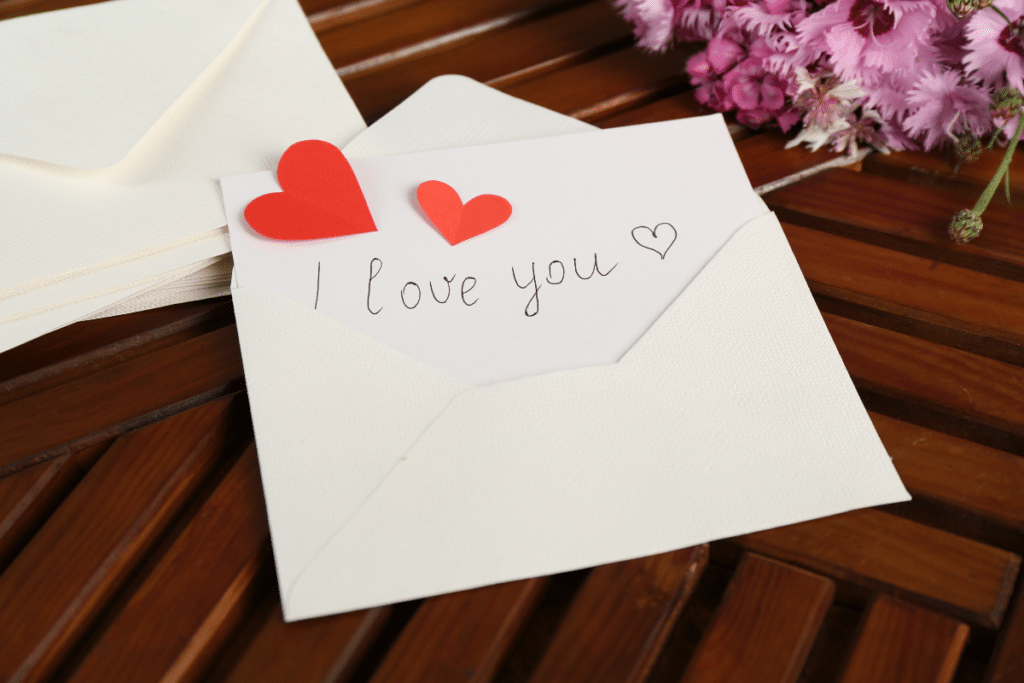 Card with phrase ‘I Love You’, red hearts and flowers on a wooden table